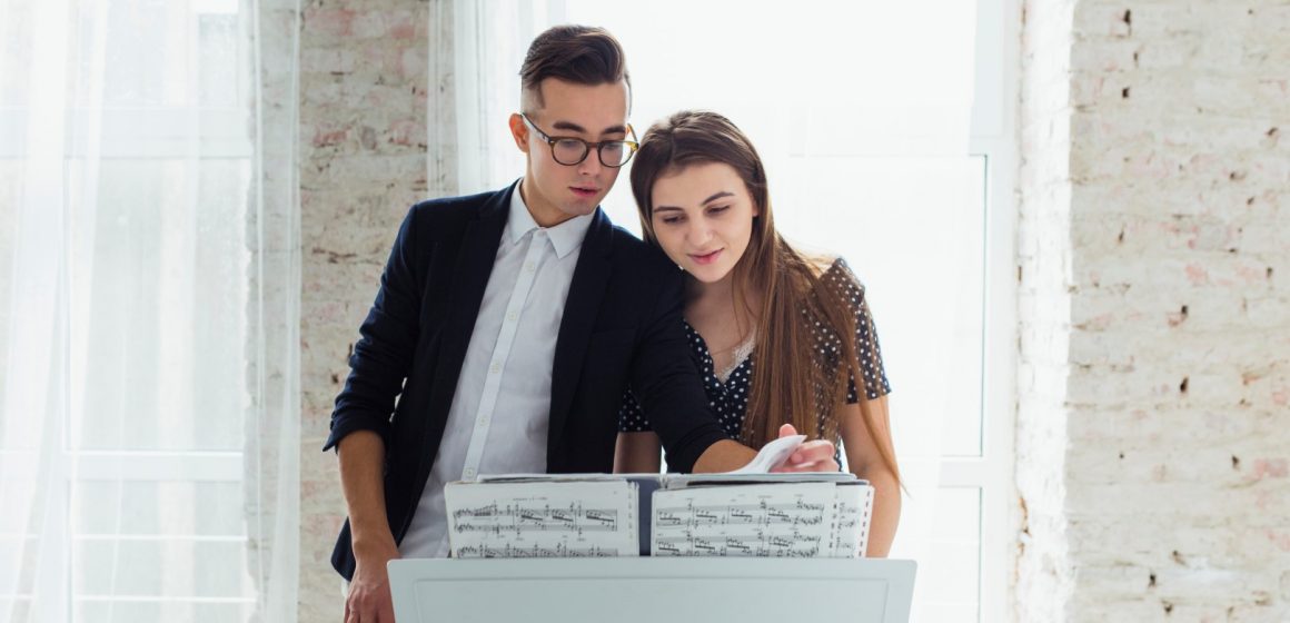 portrait-of-young-couple-looking-at-musical-sheet-learning-to-play-the-piano El reto de estudiar canto a distancia